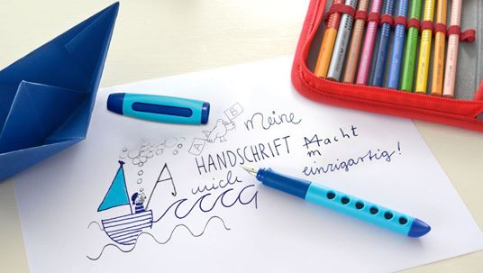 blue fountain pen for kids on a white paper with writings on it an a drawn ship and a red pencil case and a blue paper boat