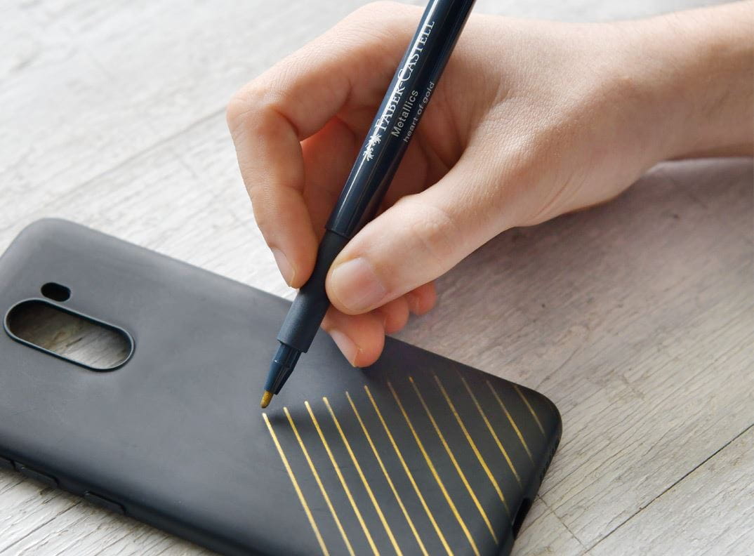 A smartphone case getting painted with a gold metallics pen.